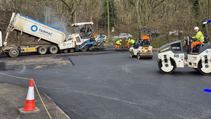 Wide shot of Tarmac dumper truck pouring new asphalt onto road with hi-vis jacketed workers in foreground