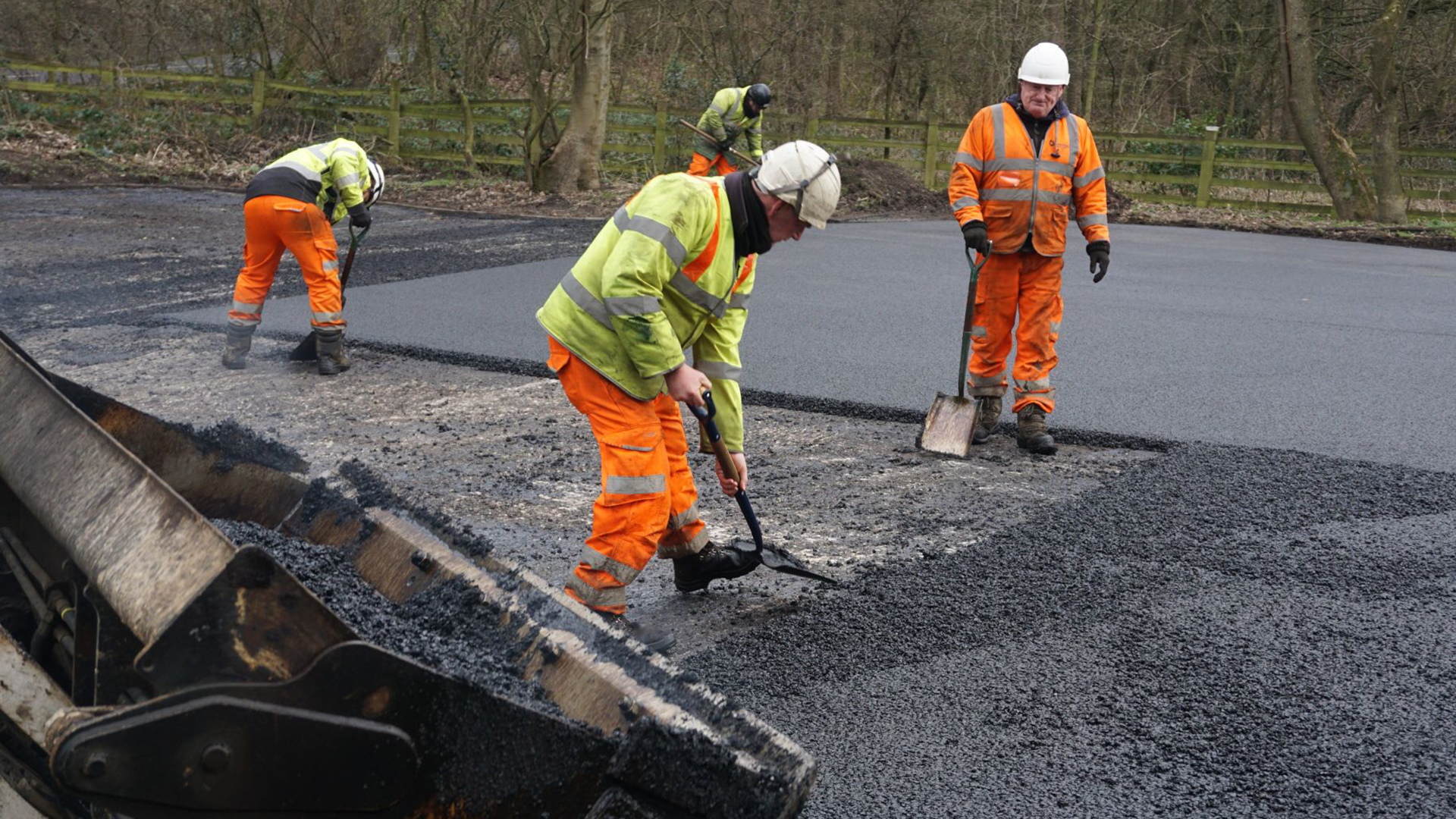 Tarmac workers in hi-vis uniforms laying down graphene-based asphalt manually