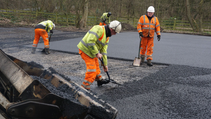 Tarmac workers in hi-vis uniforms laying down graphene-based asphalt manually