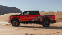 A red and black Ram TRX with graphic details, parked on sand dunes with mountains in the background.