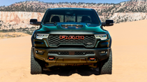 The front of a dark green Ram TRX is centred on sandy terrain, with a light-coloured mountain range in the background.