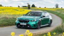 A green BMW drives on a road surrounded by a field of yellow flowers.