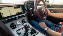 Interior of a Bentley car with leather dashboard, navigation system display, and a driver behind the wheel.
