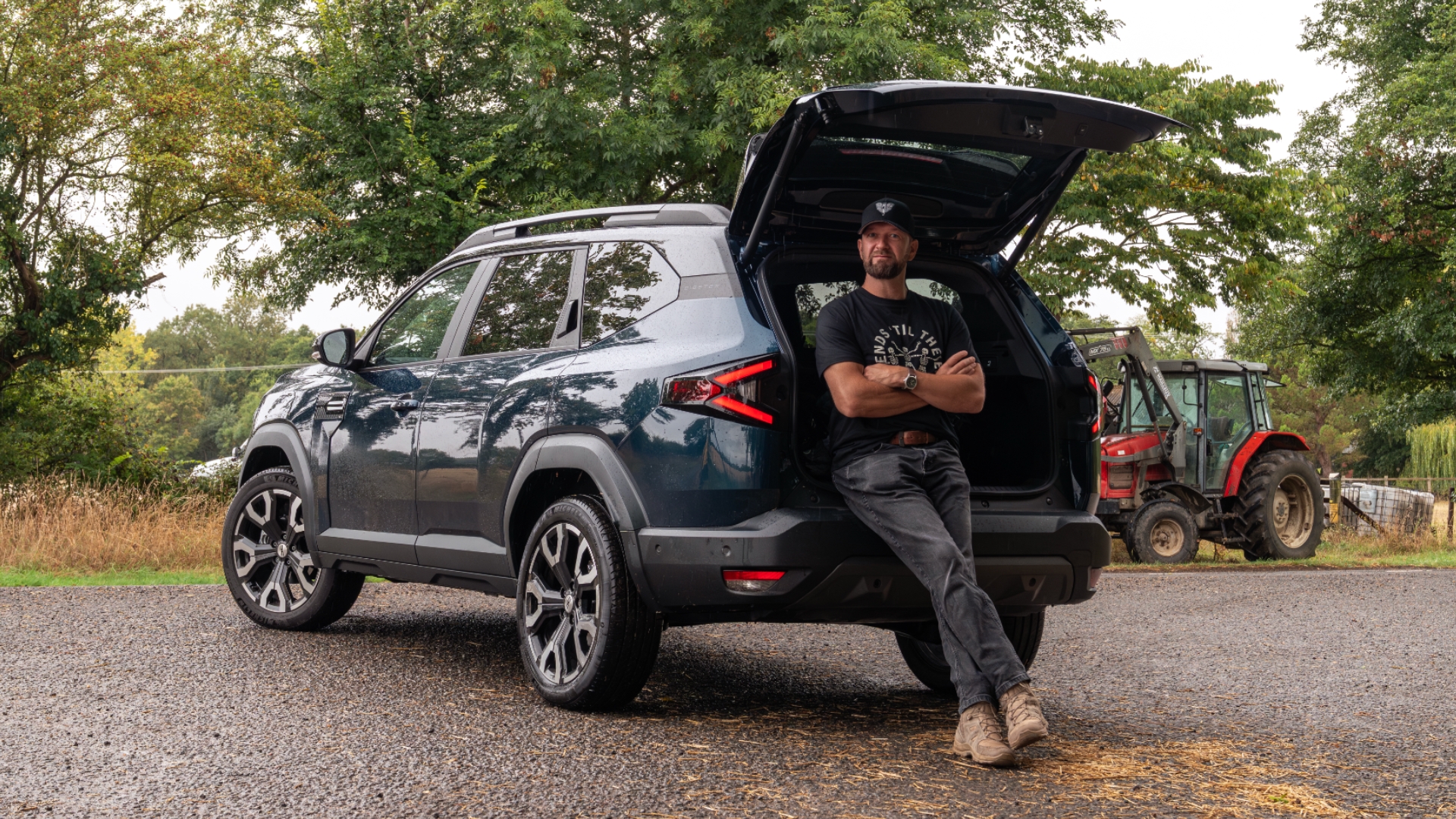 Dacia Bigster Hybrid parked outside with the boot up and driver leaning up against the car