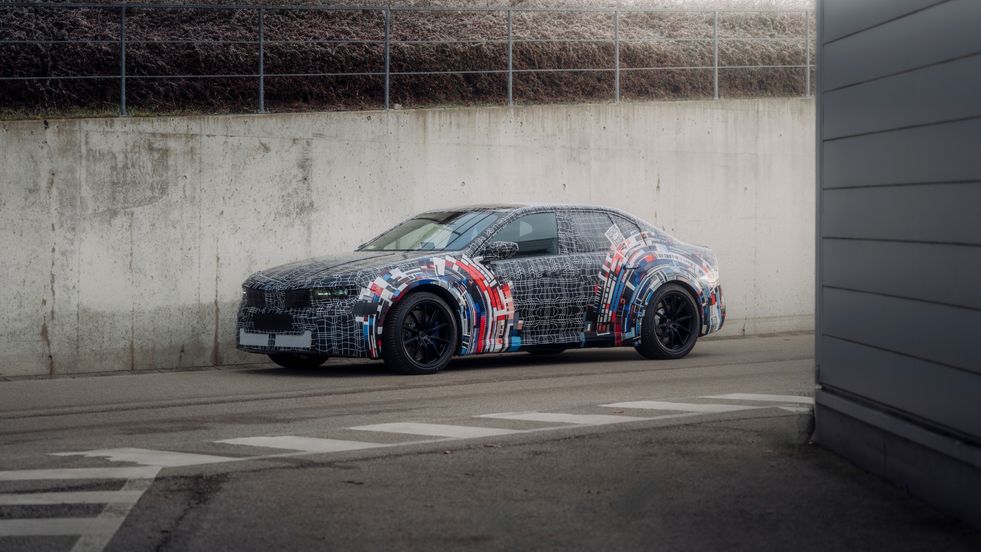 BMW M Neue Klasse parked on a road against a cement wall.