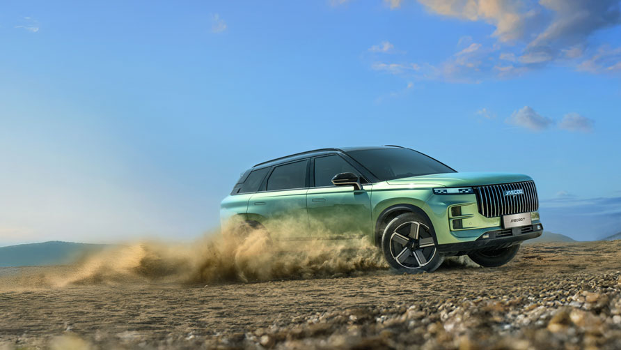 A sleek, green, hybrid JAECOO 7 SUV speeds down a dusty country road lined with trees. The sky is partly cloudy
