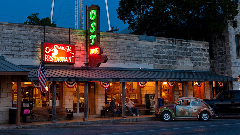 The exterior of Old Spanish Trail Restaurant, featuring a vibrant neon sign illuminating its facade at night 
