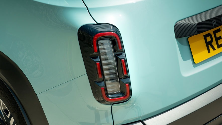 Close-up of a pastel blue Renault 4 E-Tech electric car's rear light featuring a modern, rectangular design with red accents. The yellow license plate is partially visible