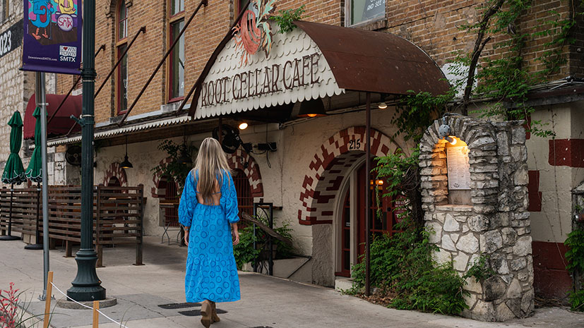 A woman in a blue dress walking towards the entrance of the Root Cellar Cafe, San Marcos, Texas, USA
