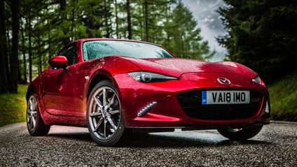 Red Mazda MX-5 in a close low static shot against a coniferous forest