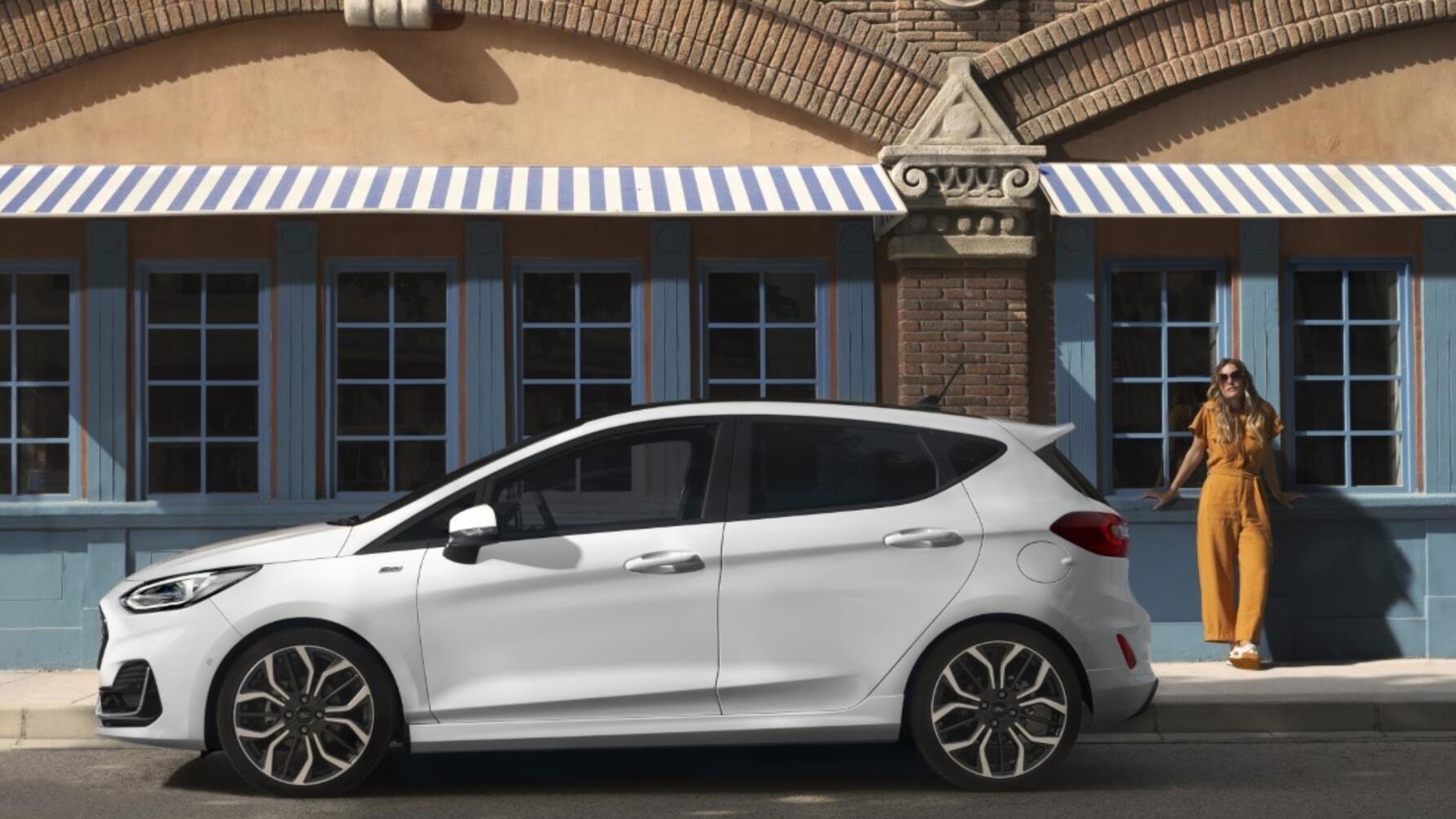 Side profile shot of white Ford Fiesta parked on street with woman in background